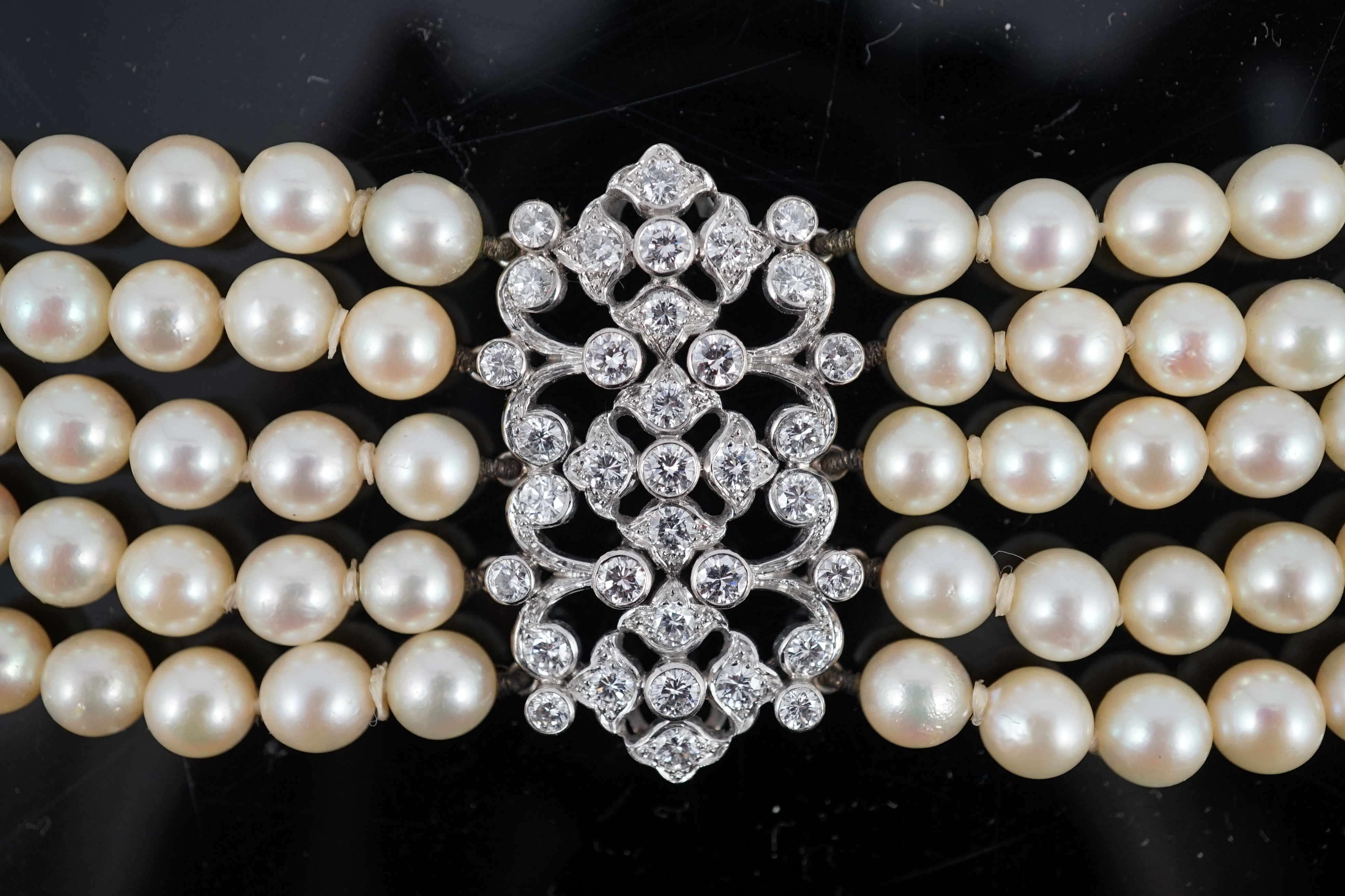 A mid 20th century quintuple strand cultured pearl choker necklace, with diamond cluster set white gold clasp and diamond cluster set white gold scrolling central motif, together with a matching bracelet